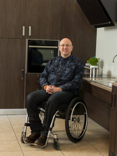 Adam Thomas in Freedom kitchen surrounded by kitchen cabinets and features whilst using a wheelchair.